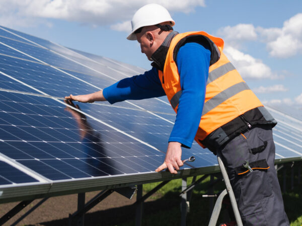 Solar power plant worker on stepladder makes a visual inspection of solar panels